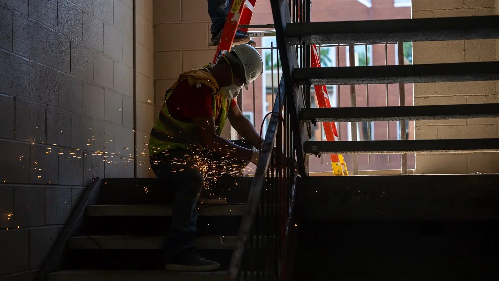 A CAMP worker using a power tool on an interior stairway with sparks visible.