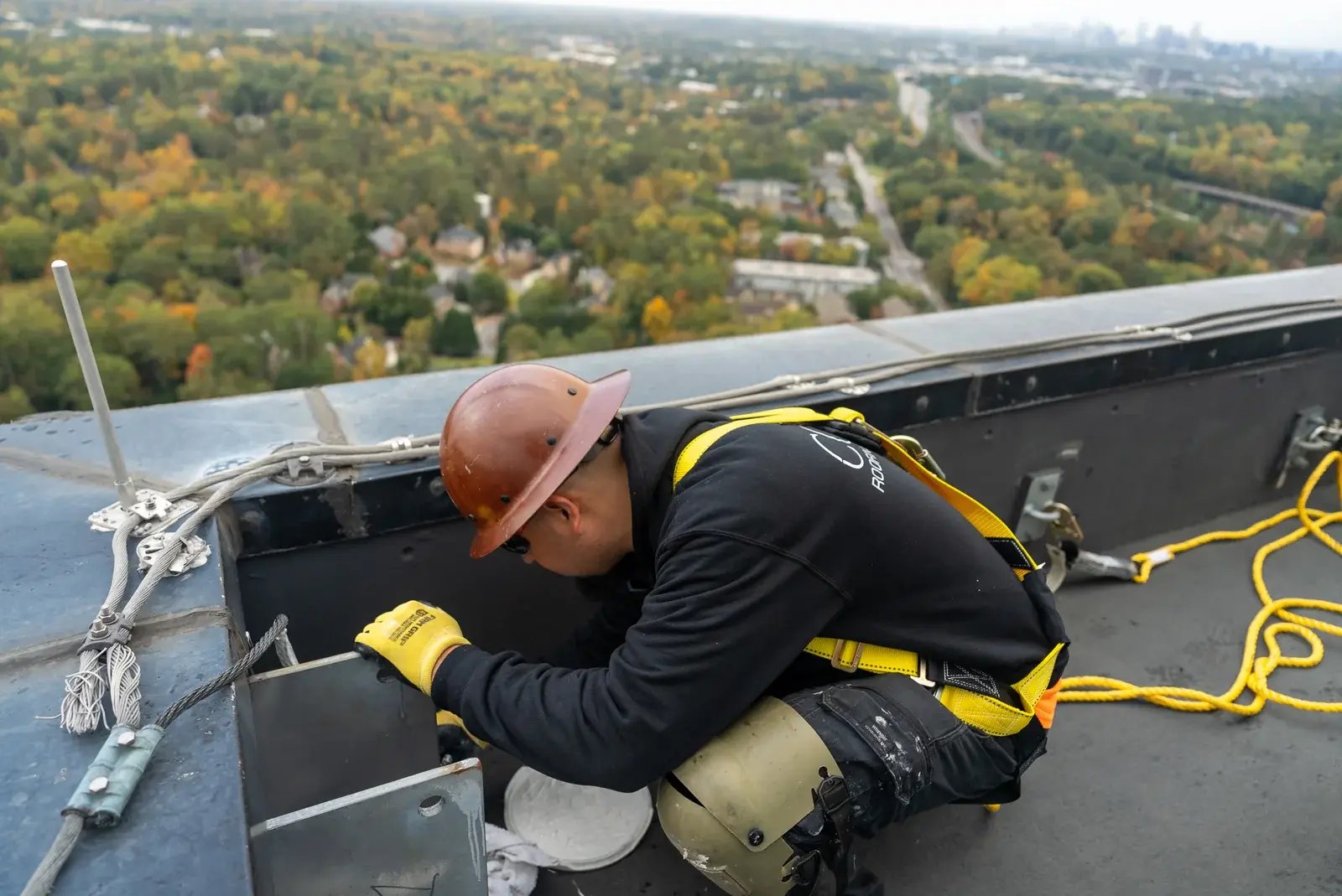 A CORE Roofing worker secured with a harness repairing the edge of a roof.
