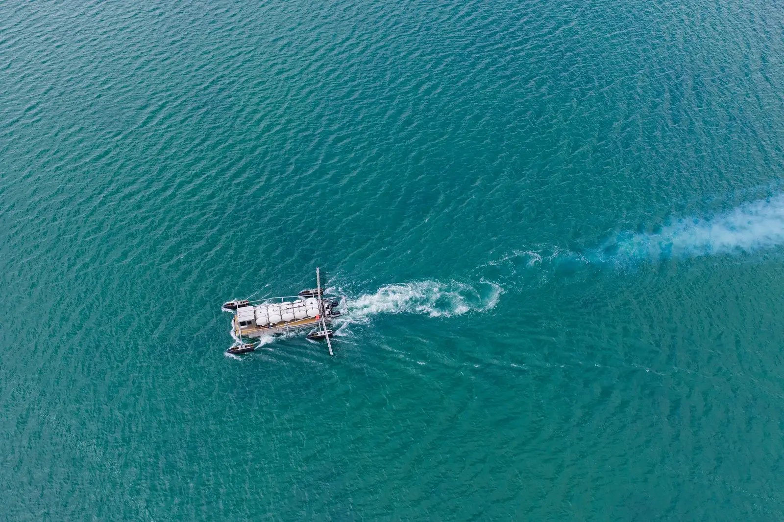 An aerial view of a workboat leaving a wake across turquoise water.