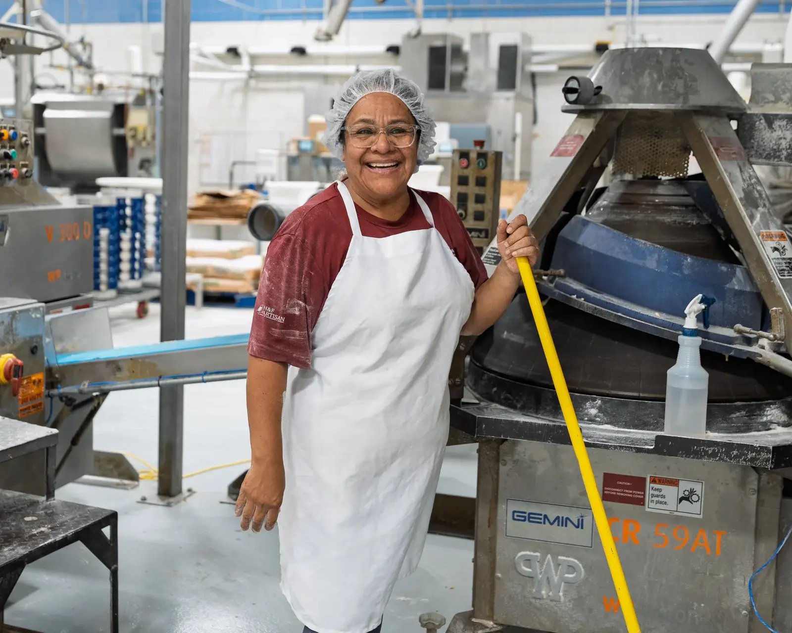 A smiling bakery staff member beside production equipment.