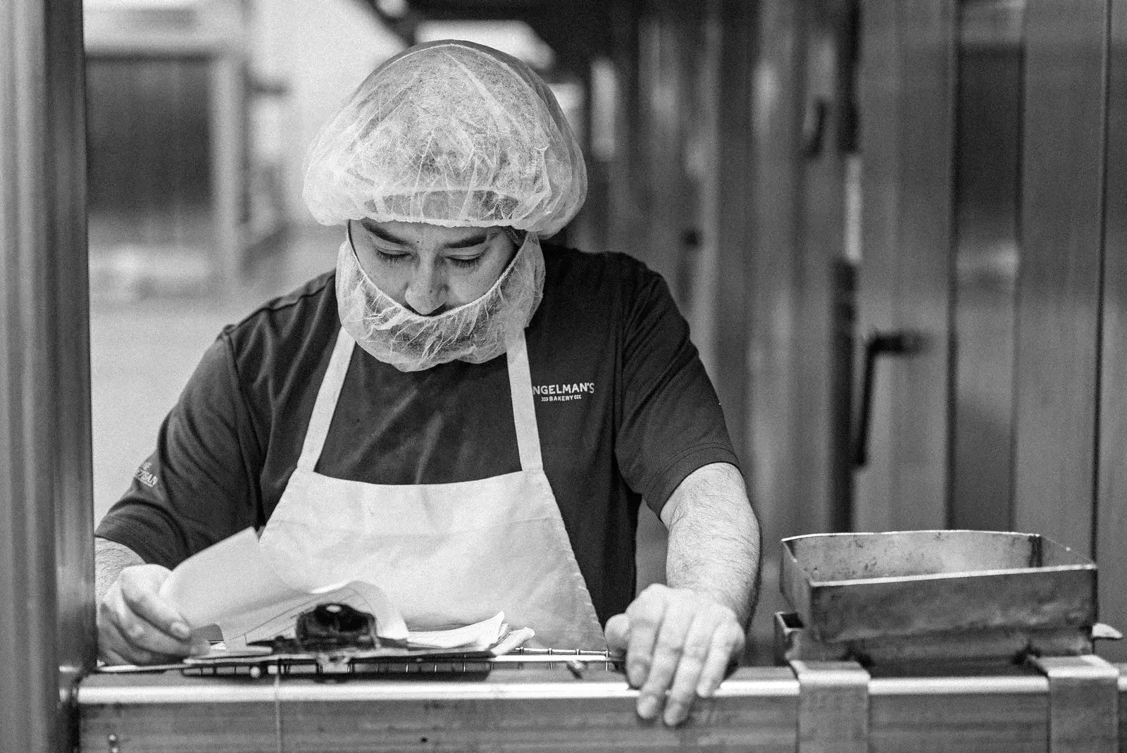 A black-and-white photograph of a bakery staff member working at a production station.