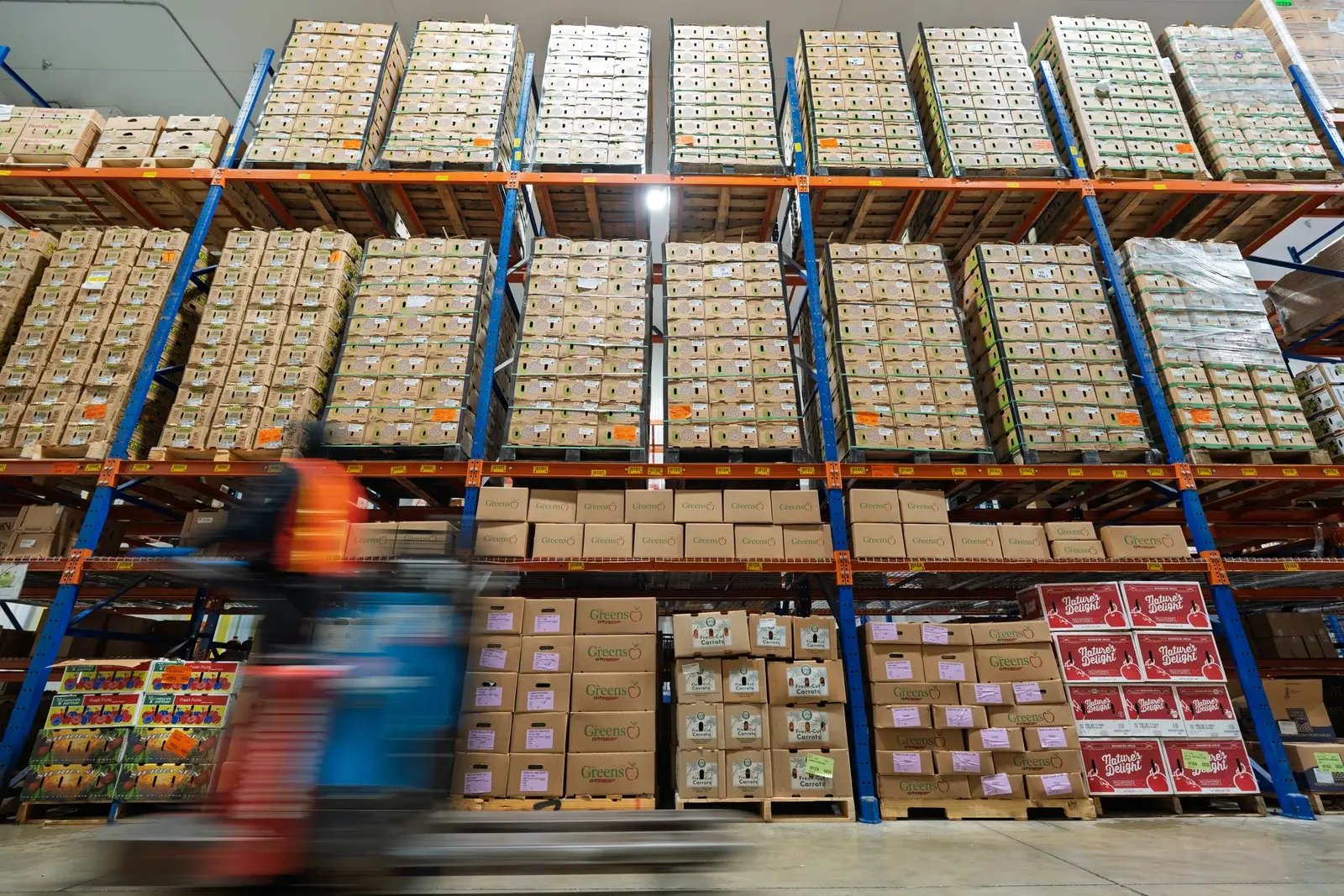 A warehouse worker passes tall racks of boxed produce in a motion-blurred photograph.