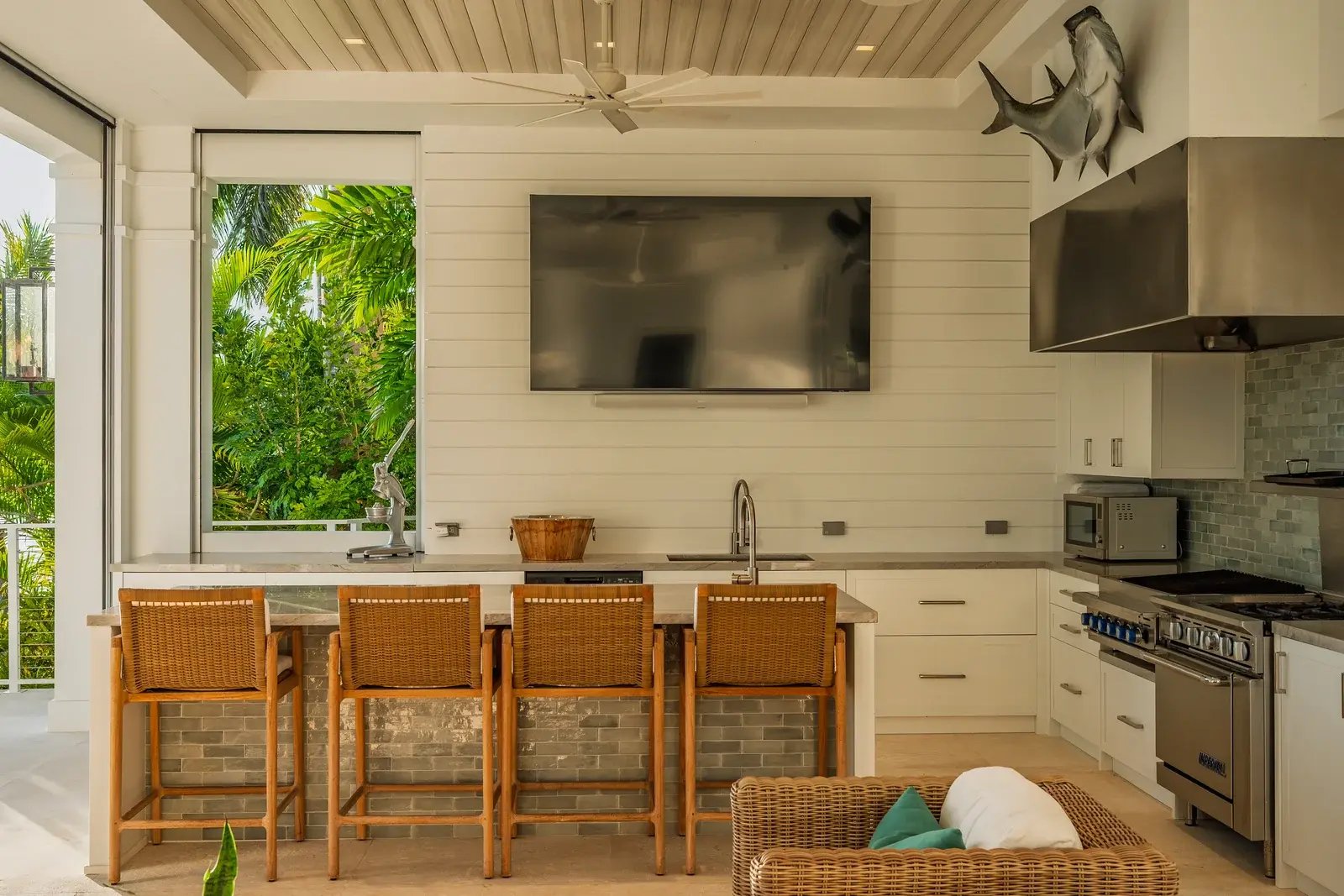 A covered outdoor kitchen and bar opening toward tropical greenery.
