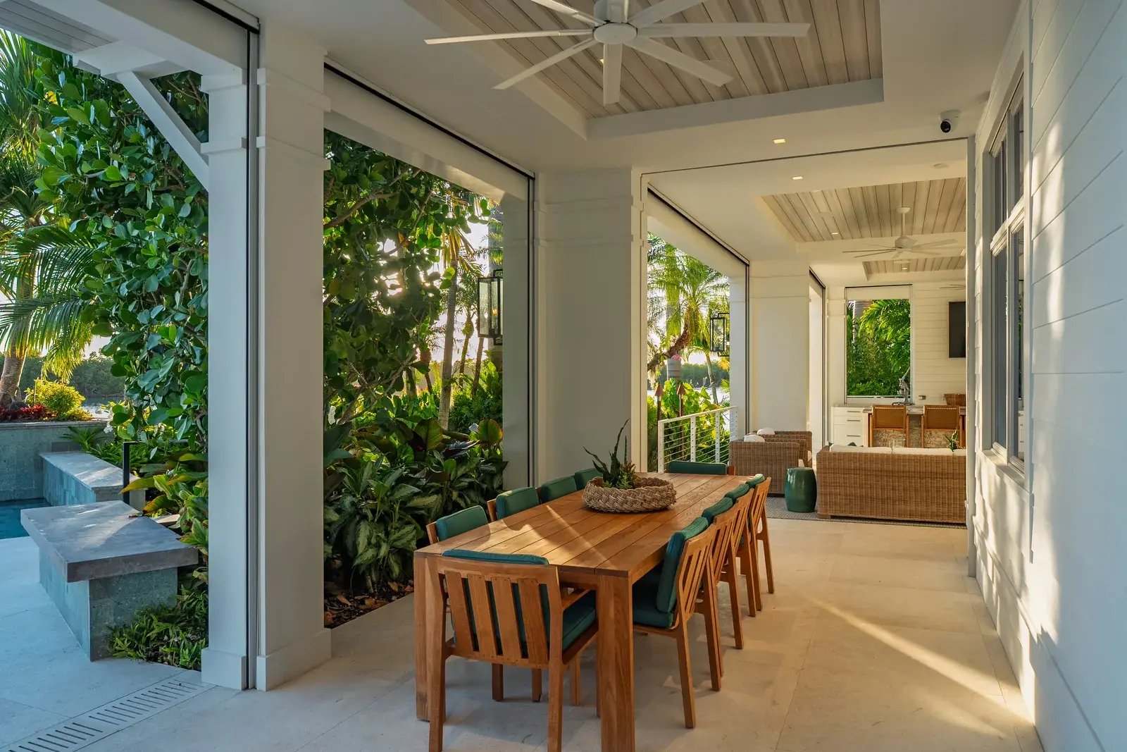 A shaded veranda with a long wooden dining table and tropical planting.