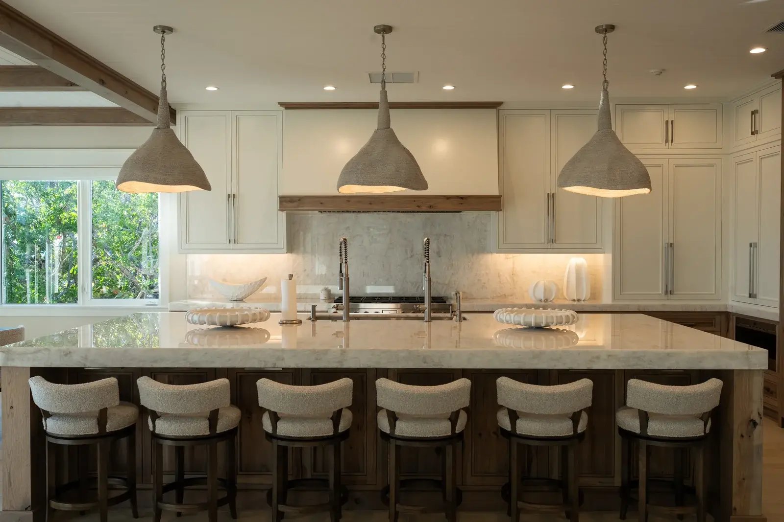 A bright kitchen with a wide island, woven bar stools and three pendant lights.