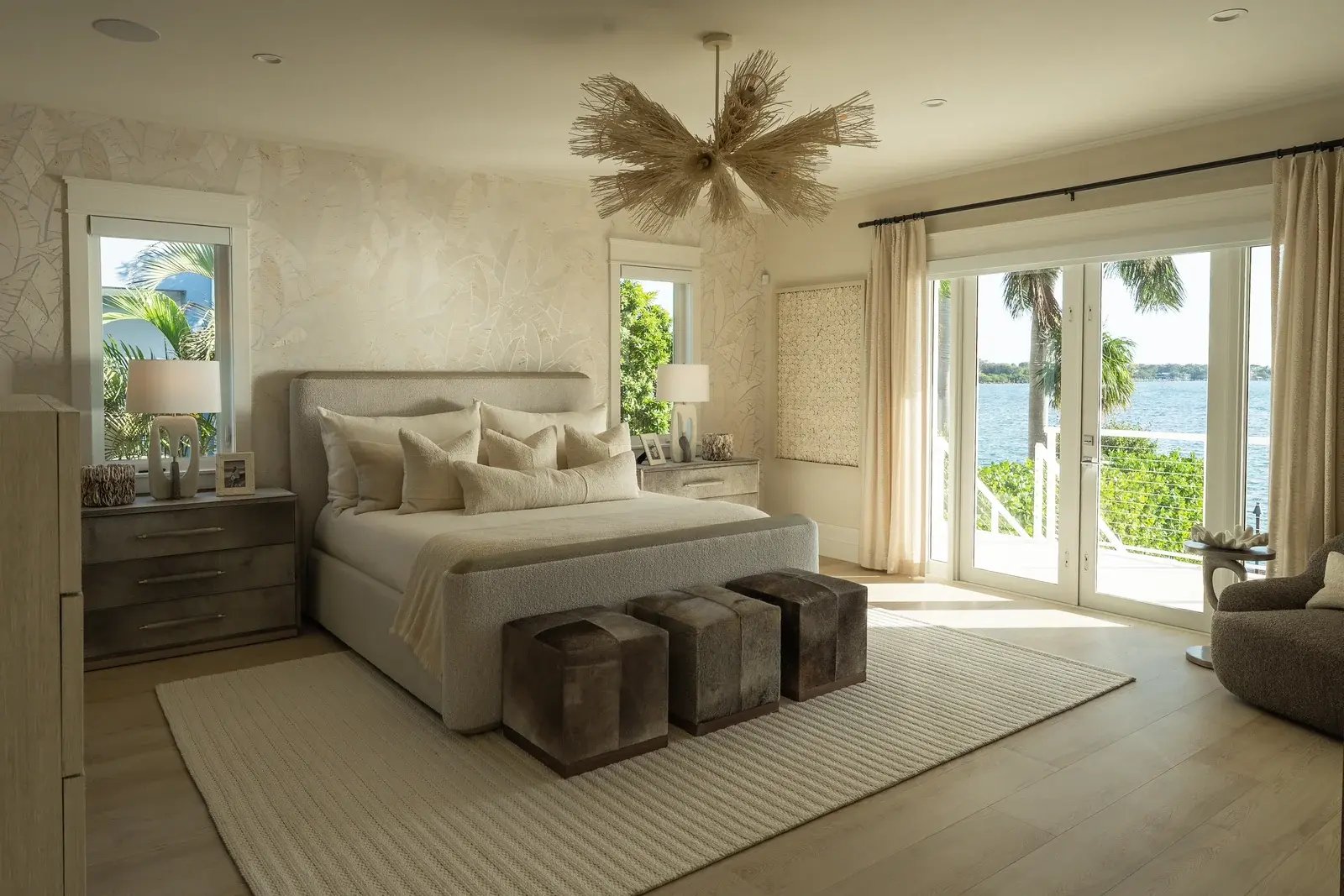 A sunlit bedroom with a canopy bed and doors opening toward the water.