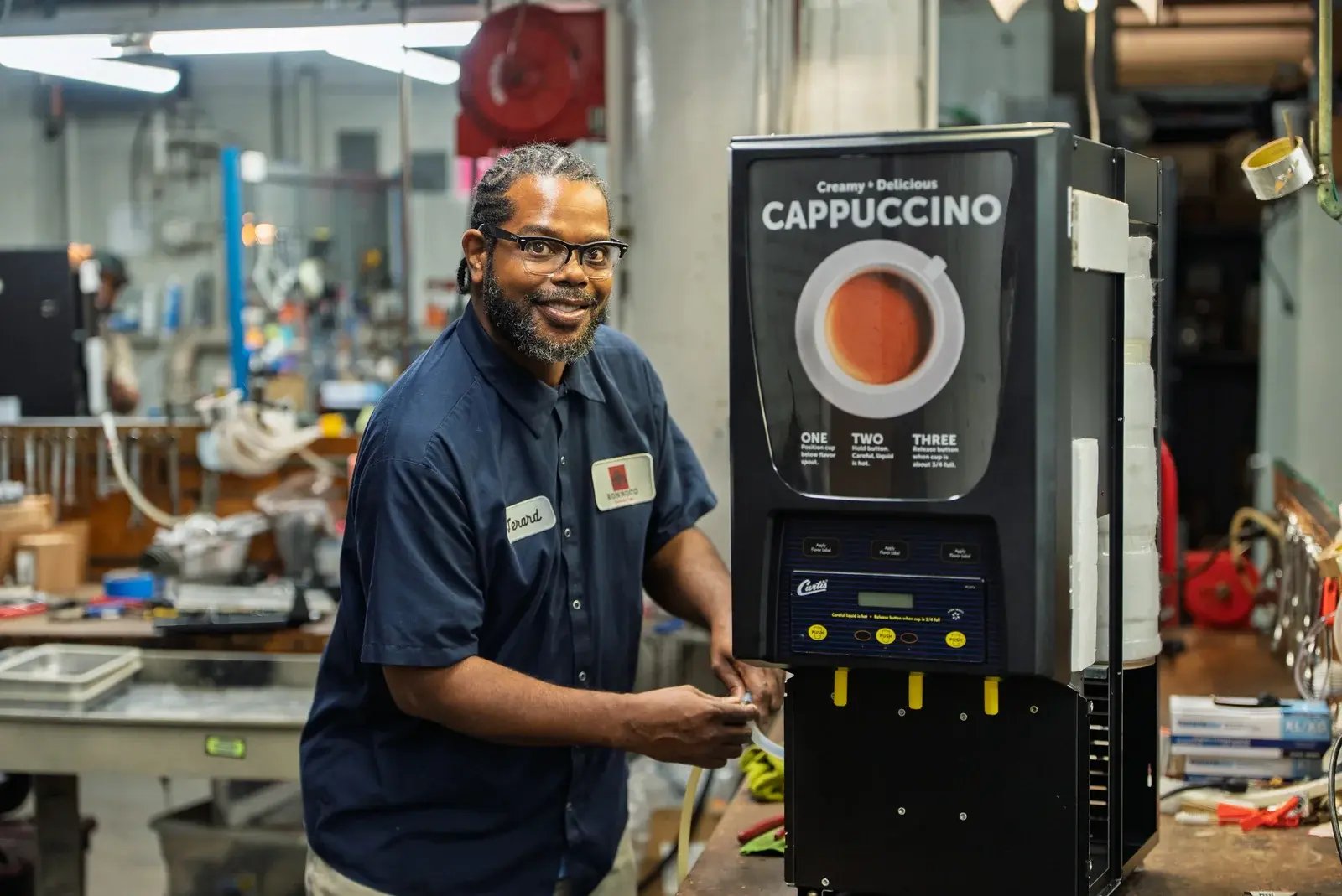 A smiling Ronnoco technician beside a cappuccino machine in a workshop.