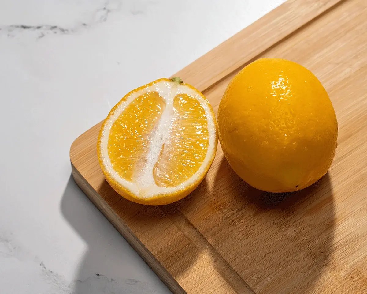 A whole yellow lemon and a cut lemon half on a wooden board.
