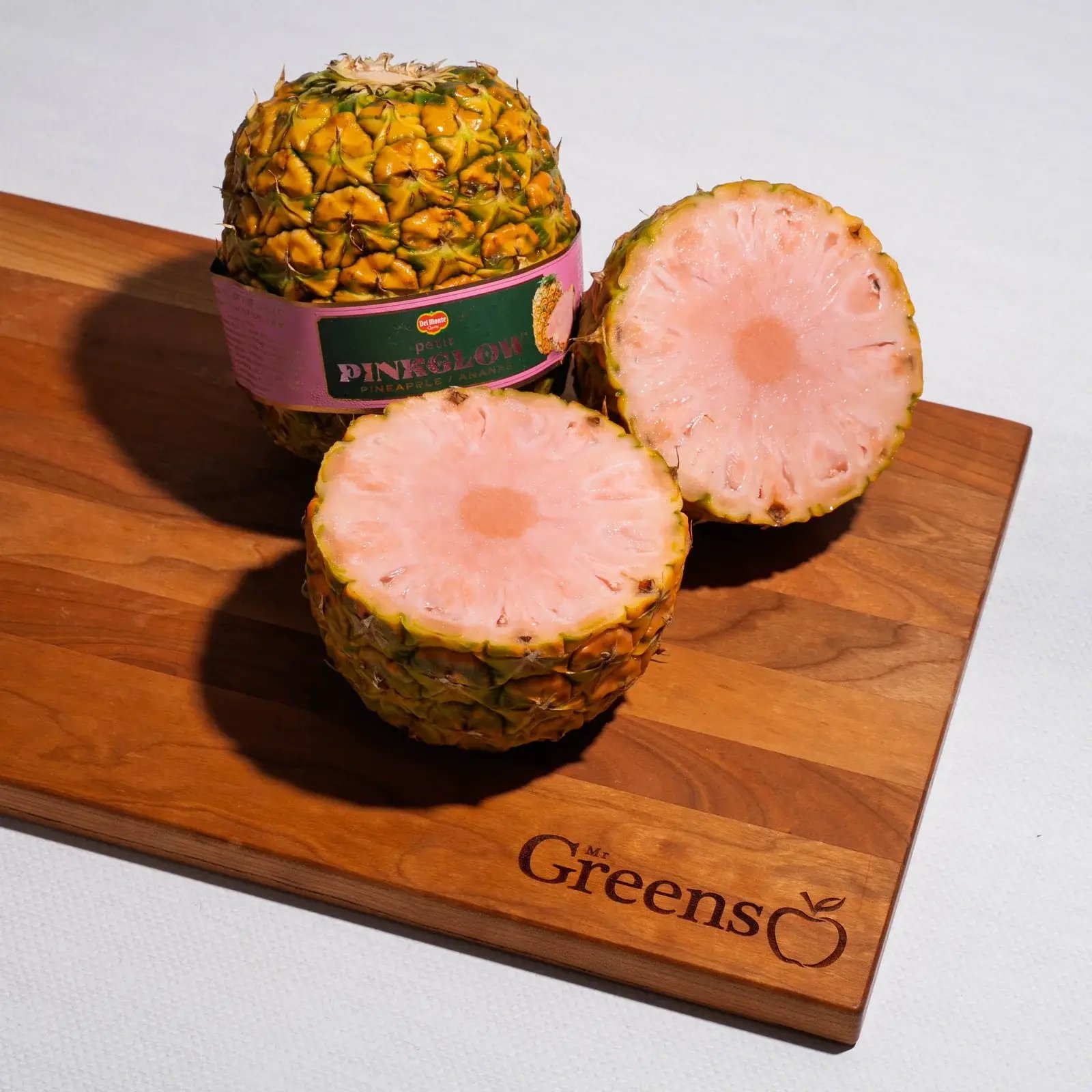 A pink-fleshed pineapple cut into sections on a wooden board in direct sunlight.
